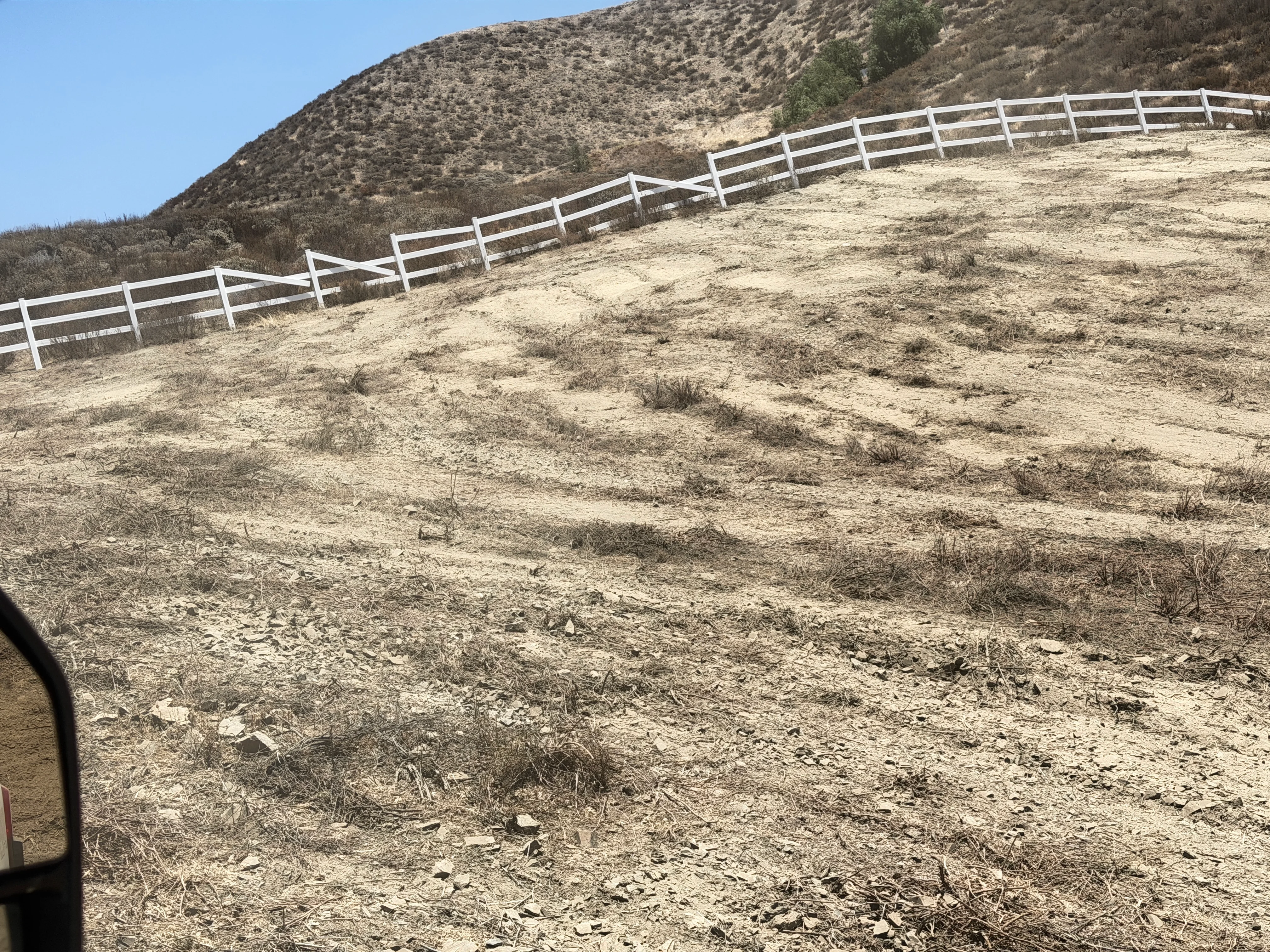Cleared hillside with white ranch fencing installed along contoured slope in Canyon Lake