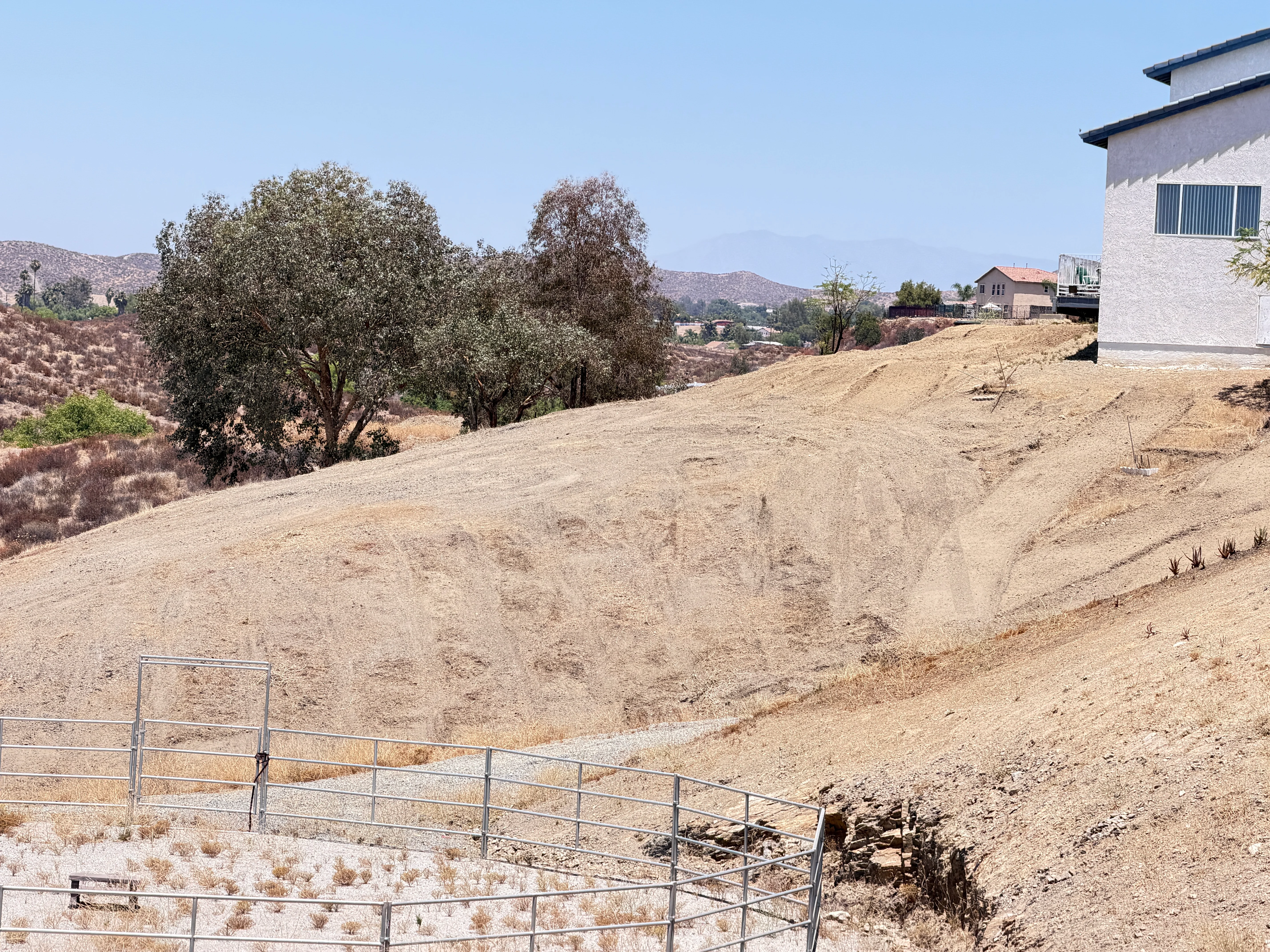 Cleared hillside lot with graded dirt, metal gate, and mature trees in Canyon Lake