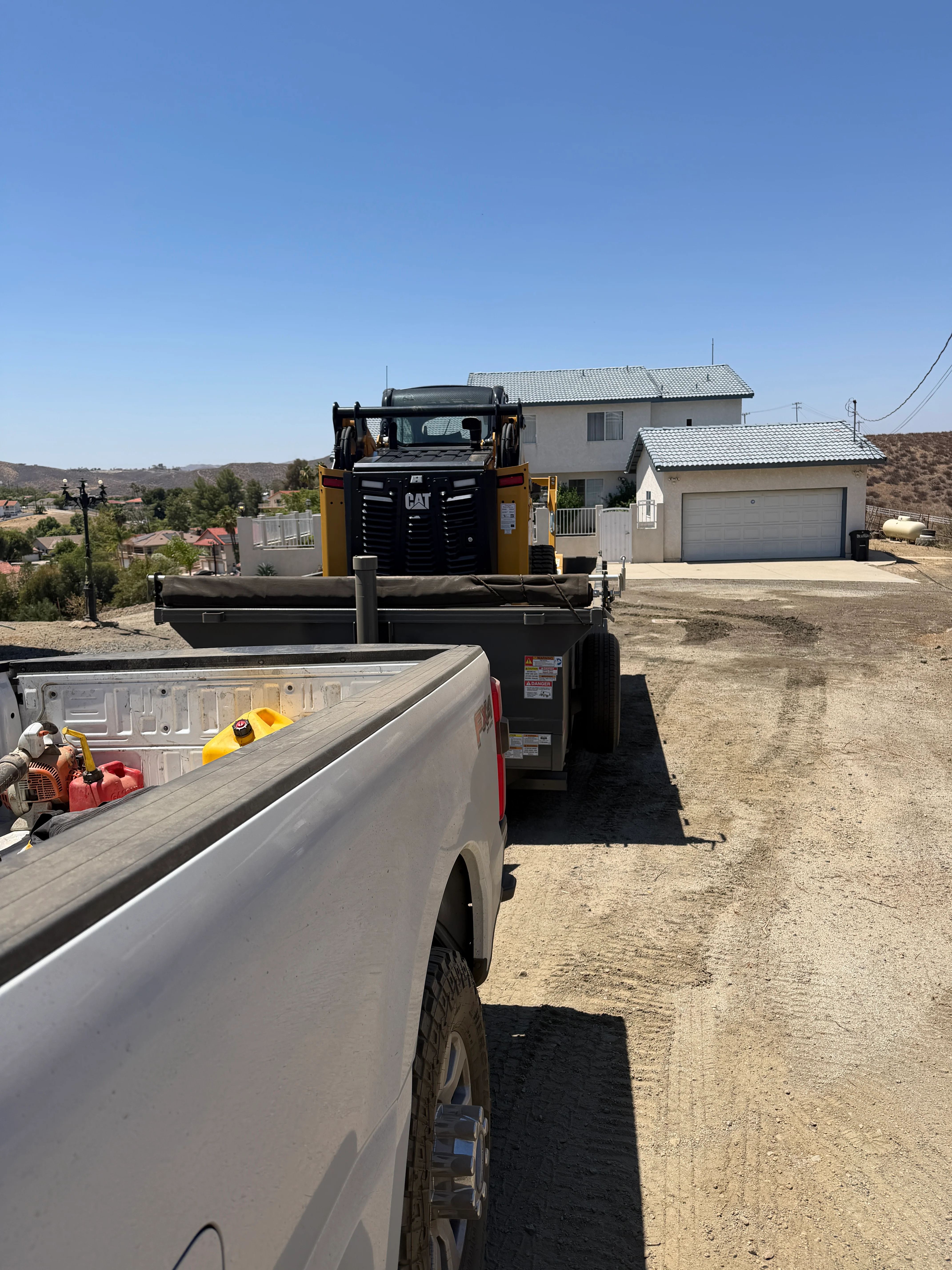 CAT skid steer loader on residential driveway with support truck and hillside home
