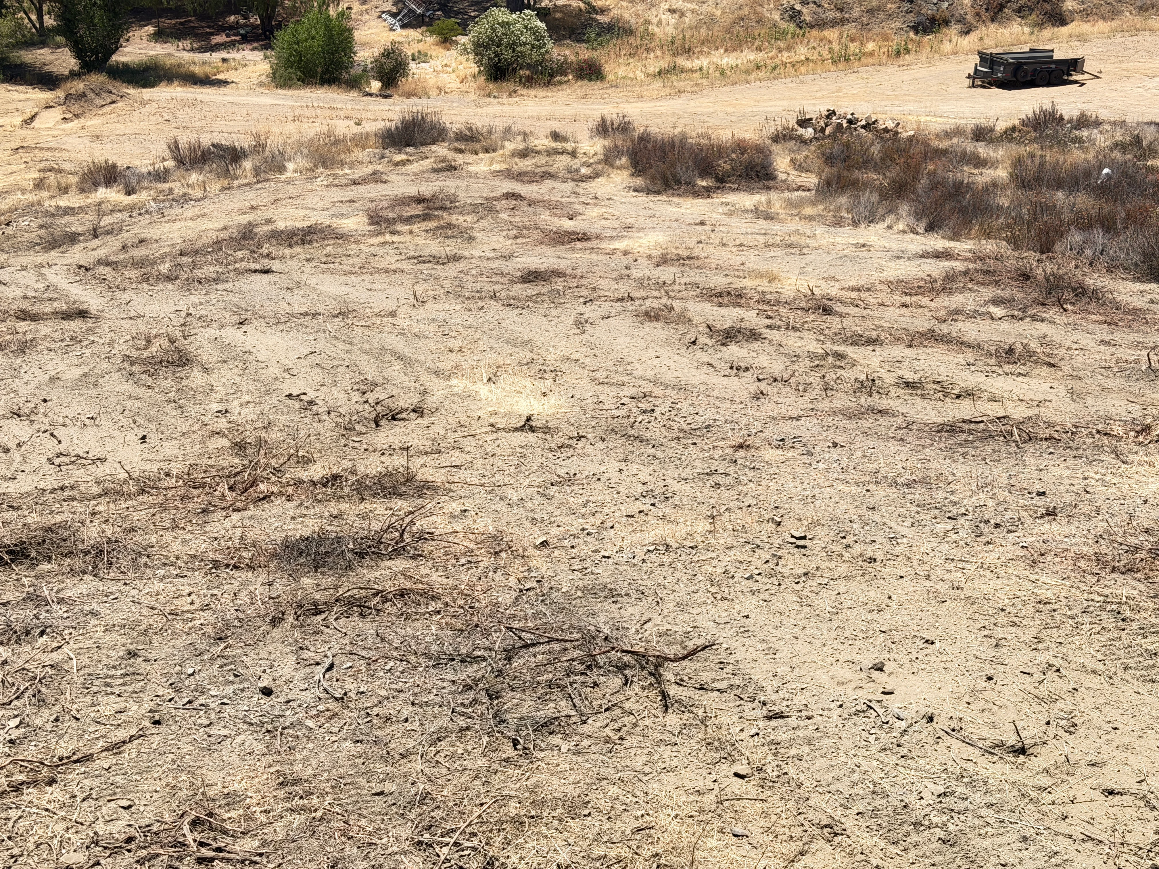 Cleared dirt lot with removed brush and debris, equipment visible in background