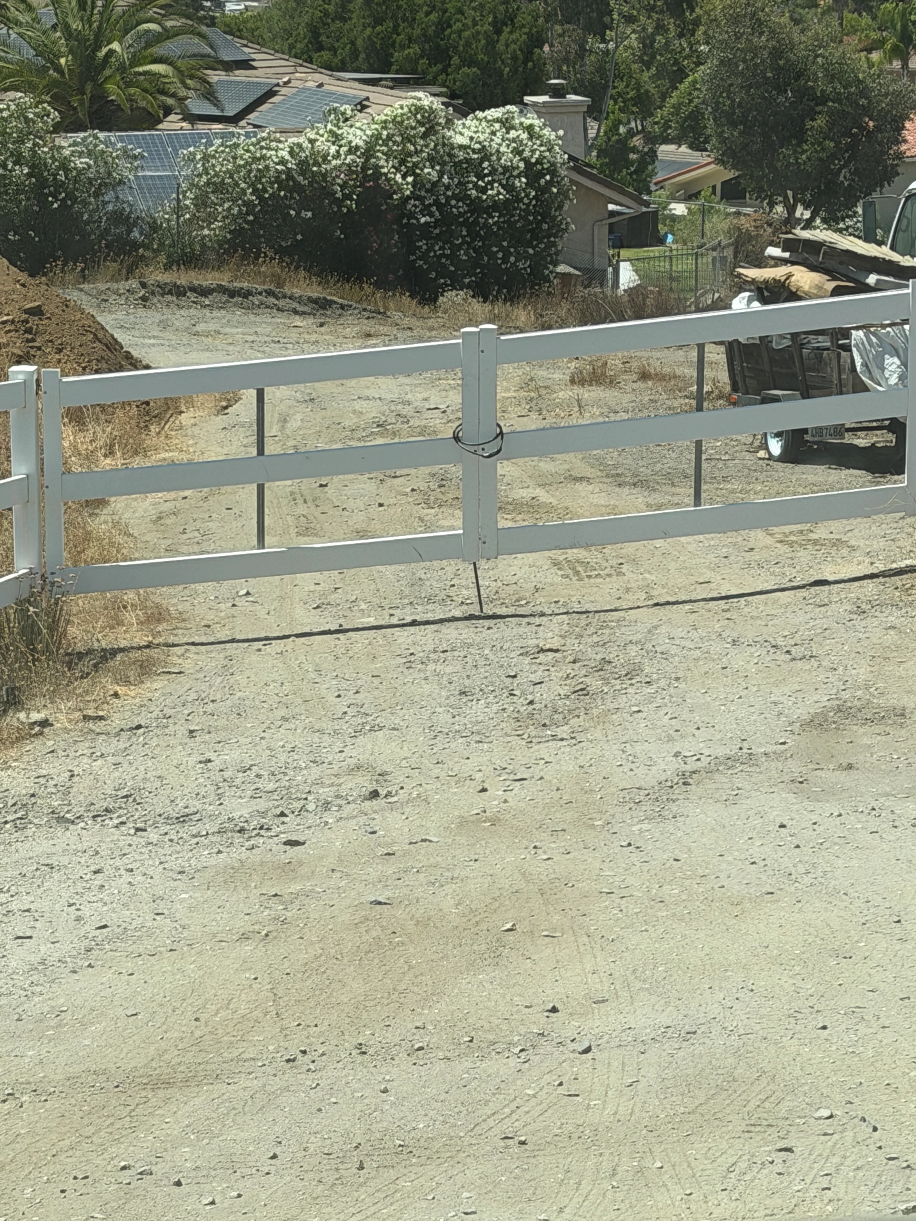 Gray metal four-rail gate installed on cleared gravel driveway with manicured landscape beyond