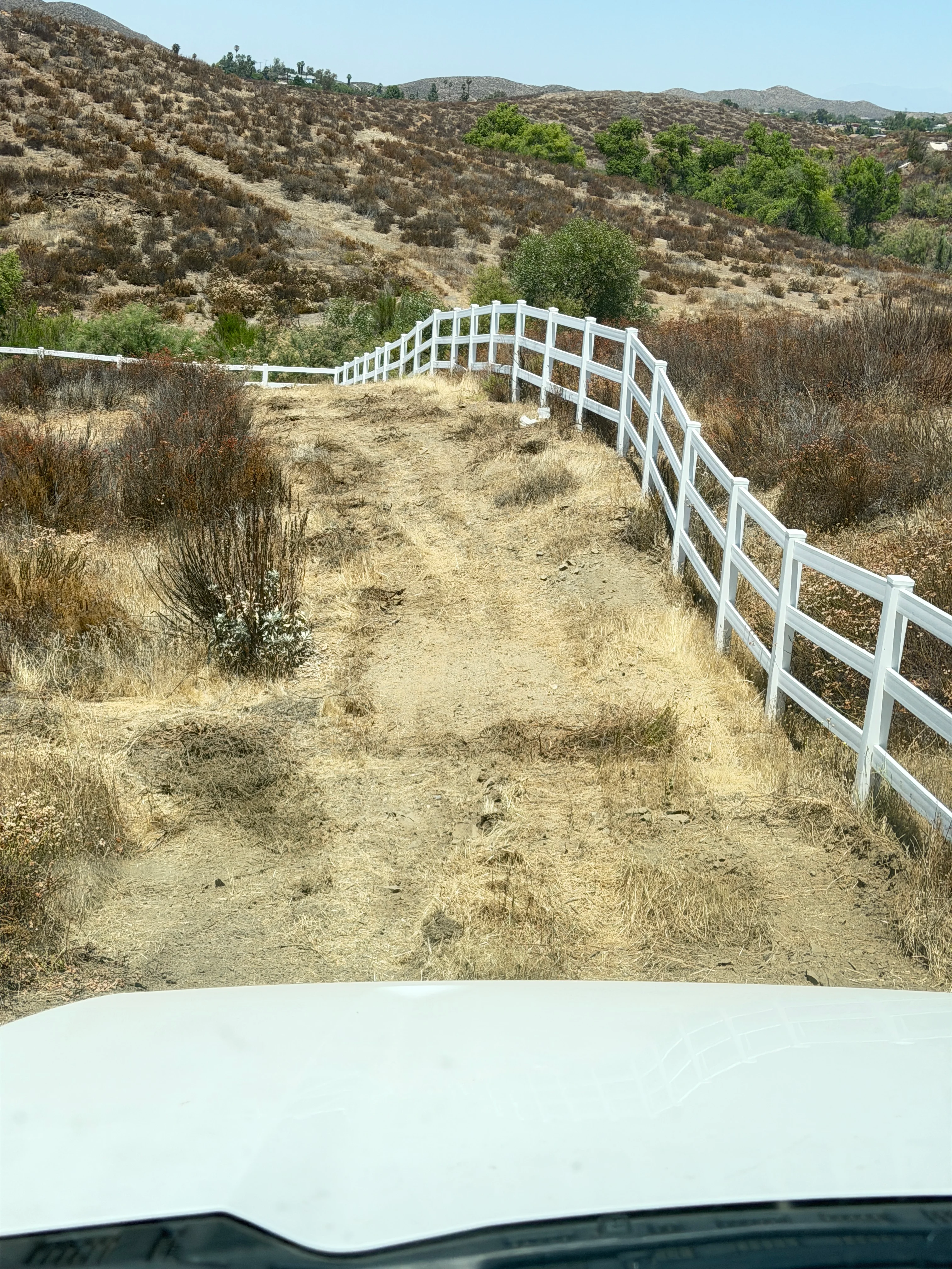 White ranch fencing installed on cleared hillside with native brush and mountains in background