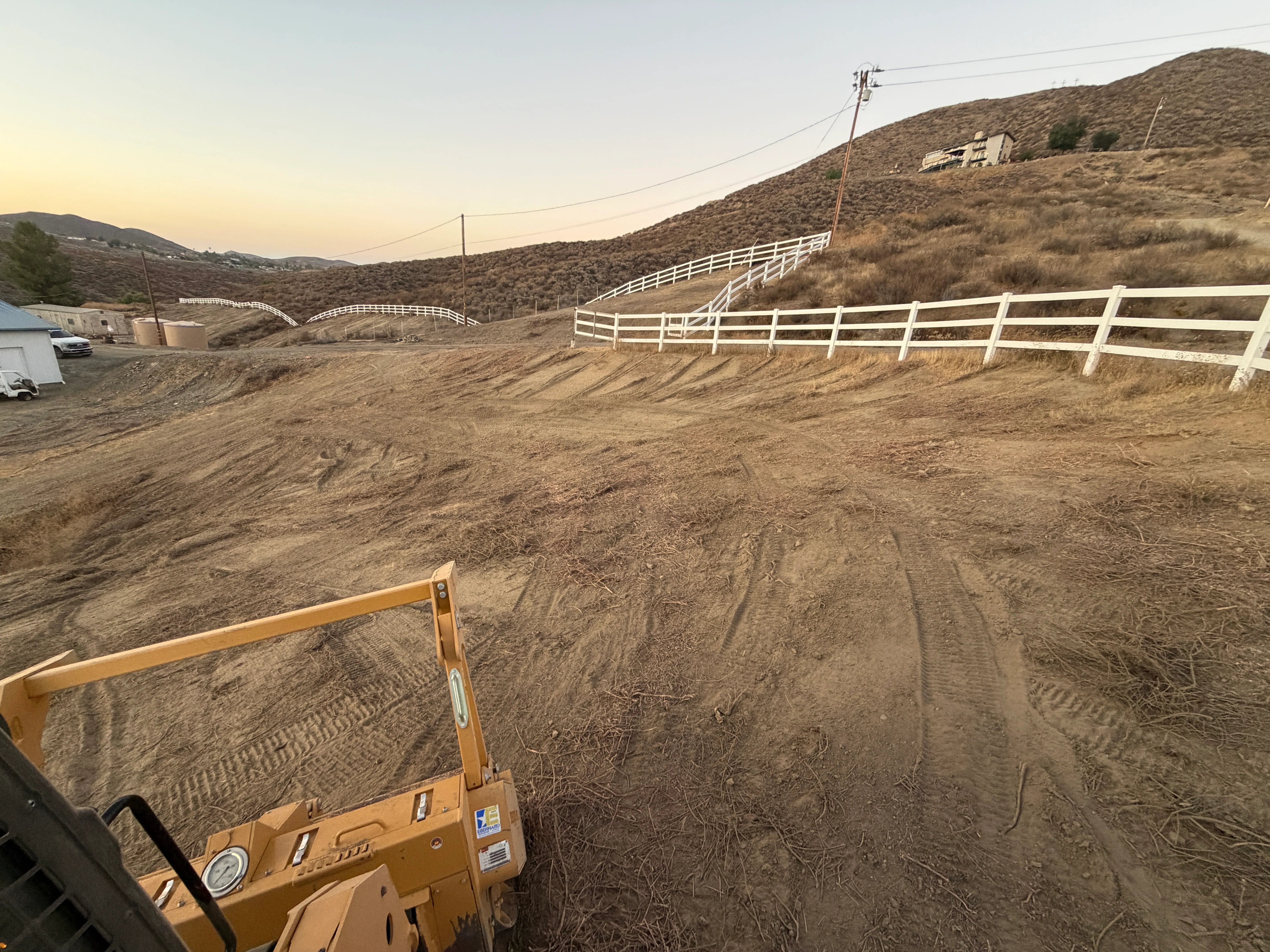 Graded ranch property with white ranch fencing and cleared hillside terrain