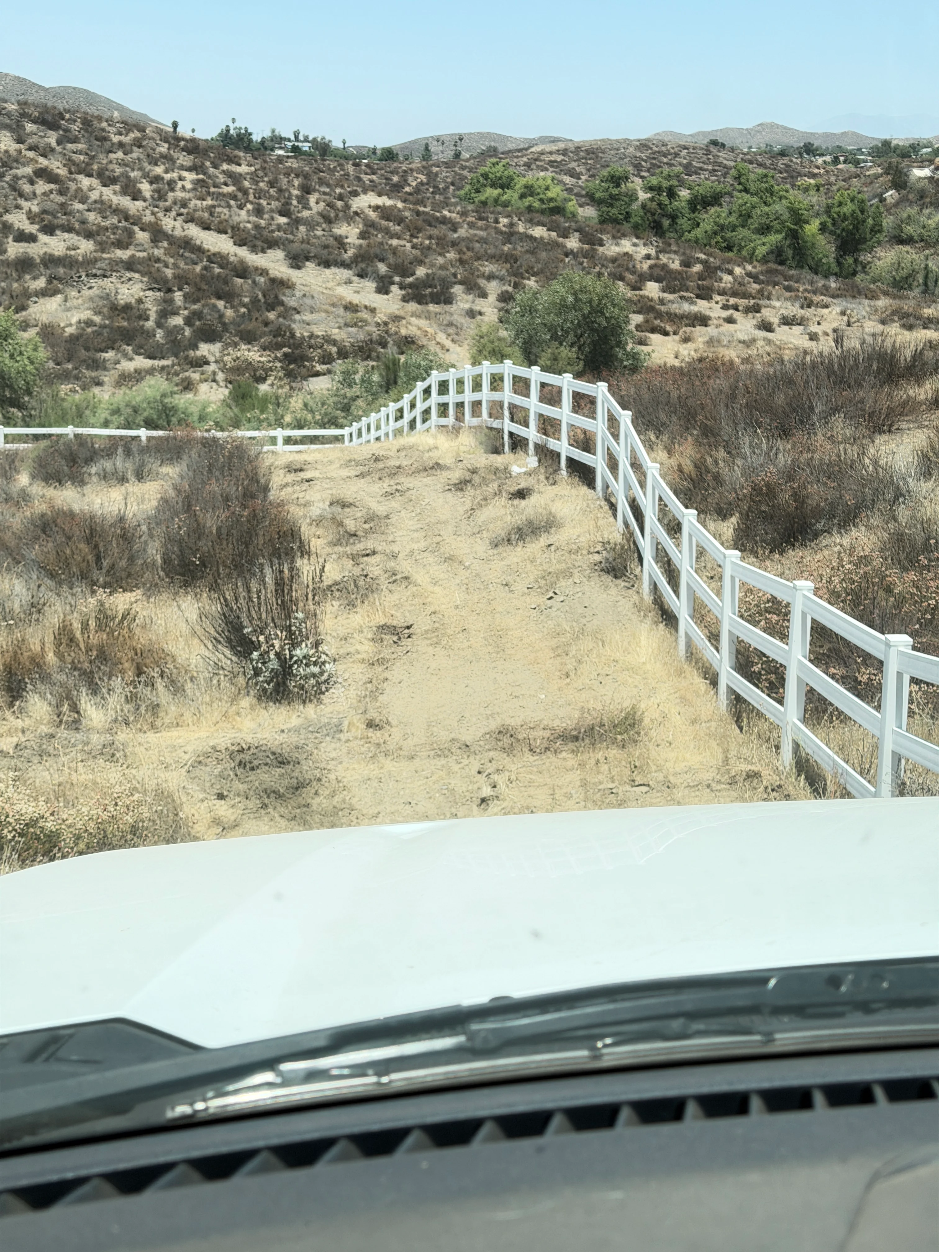 White ranch fencing installed on cleared hillside with sparse vegetation and mountains in background