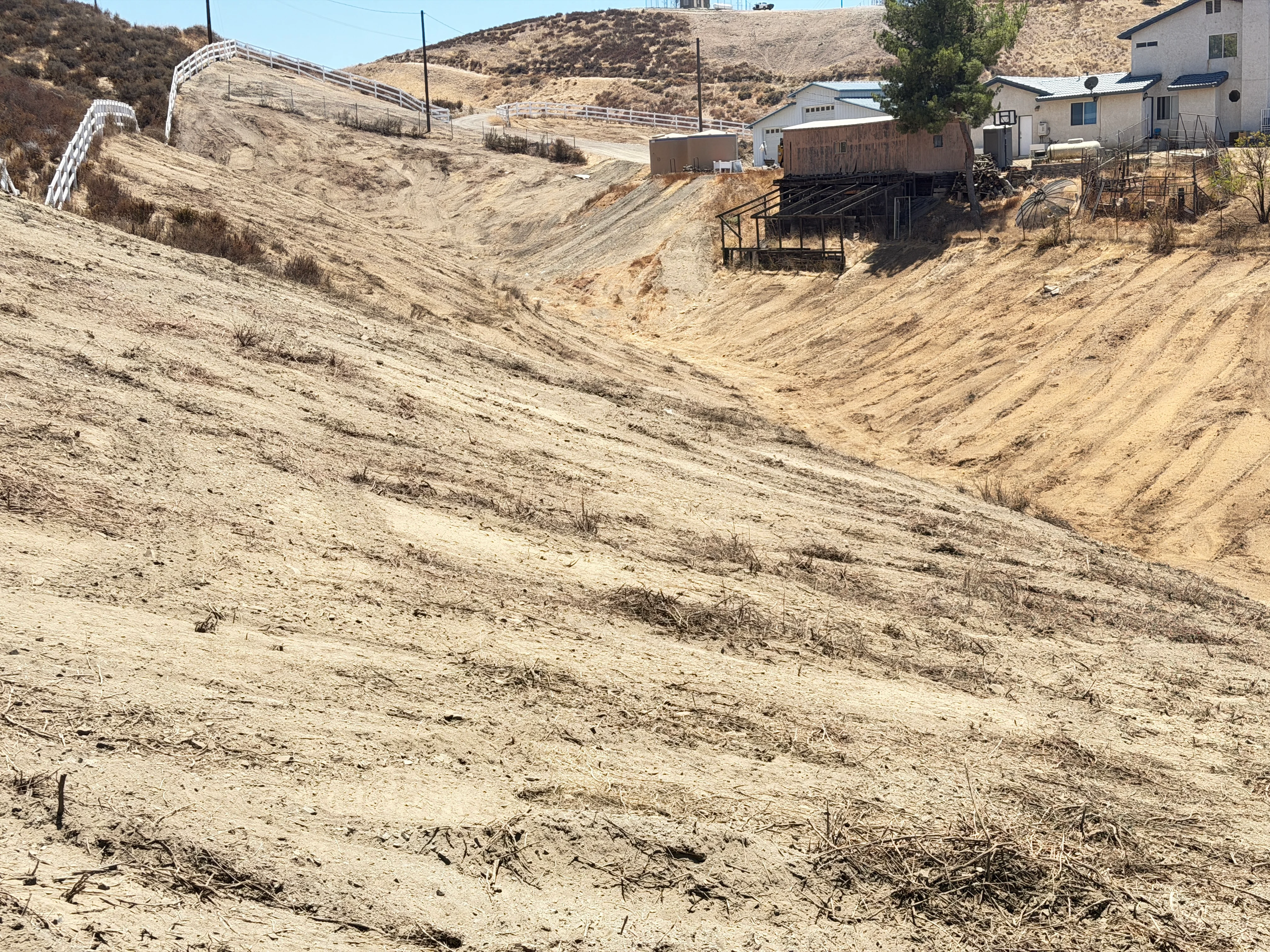 Cleared hillside with graded earth and metal fencing on residential property