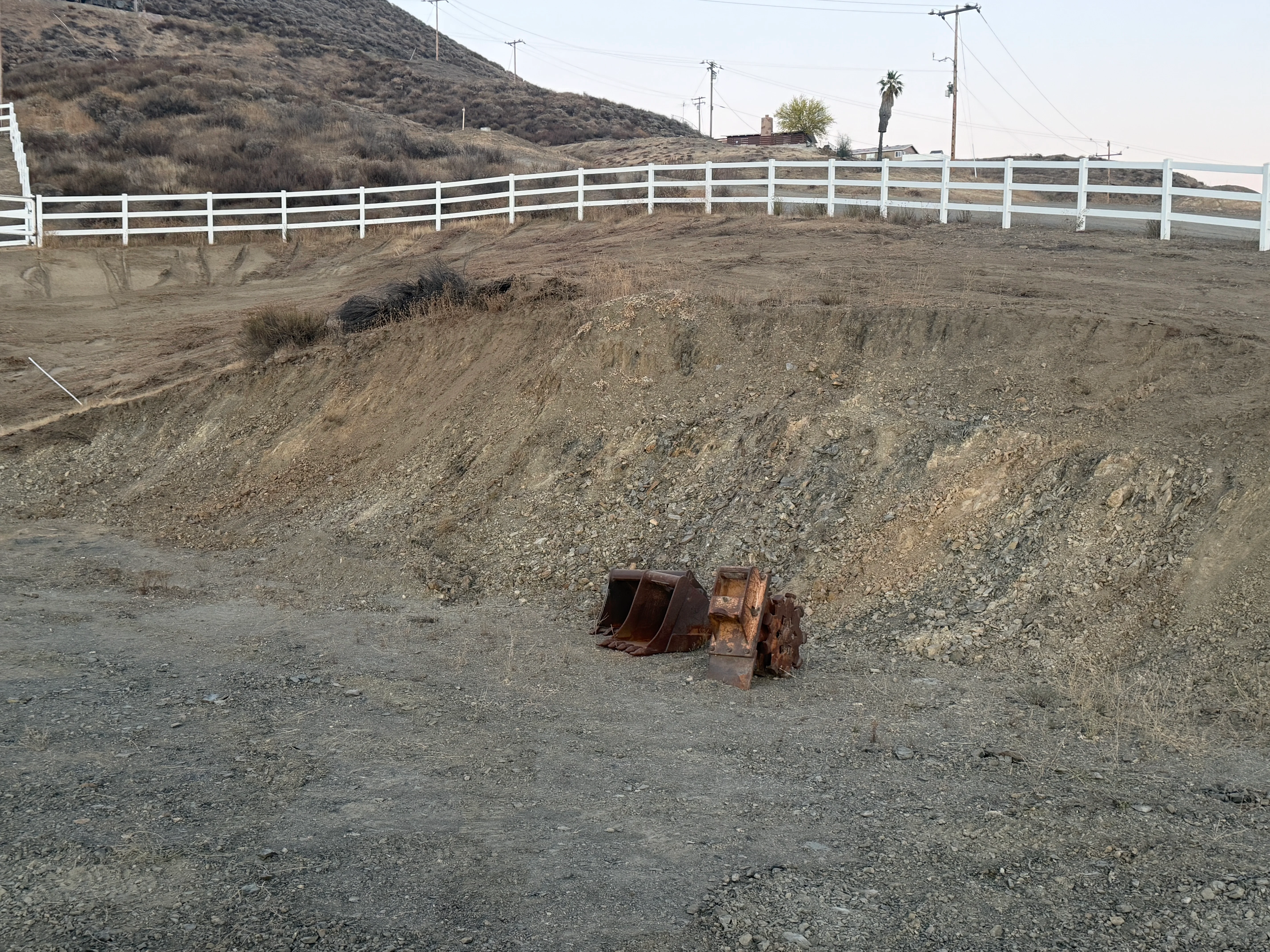 Excavated hillside with white perimeter fencing and heavy equipment bucket visible