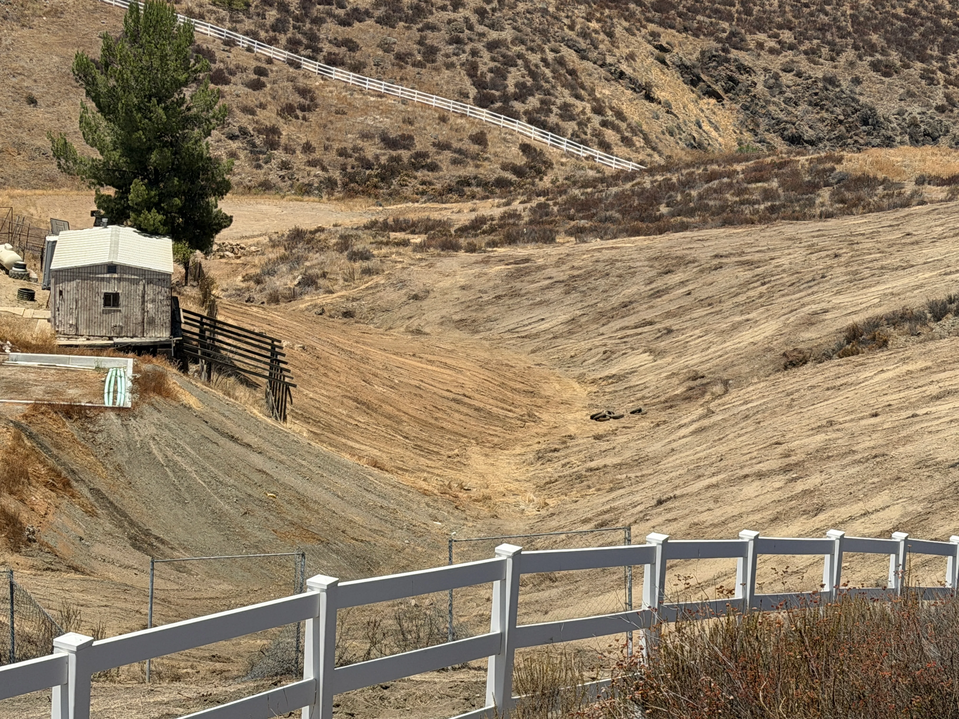 Cleared hillside with white ranch fencing and graded earth on sloped terrain