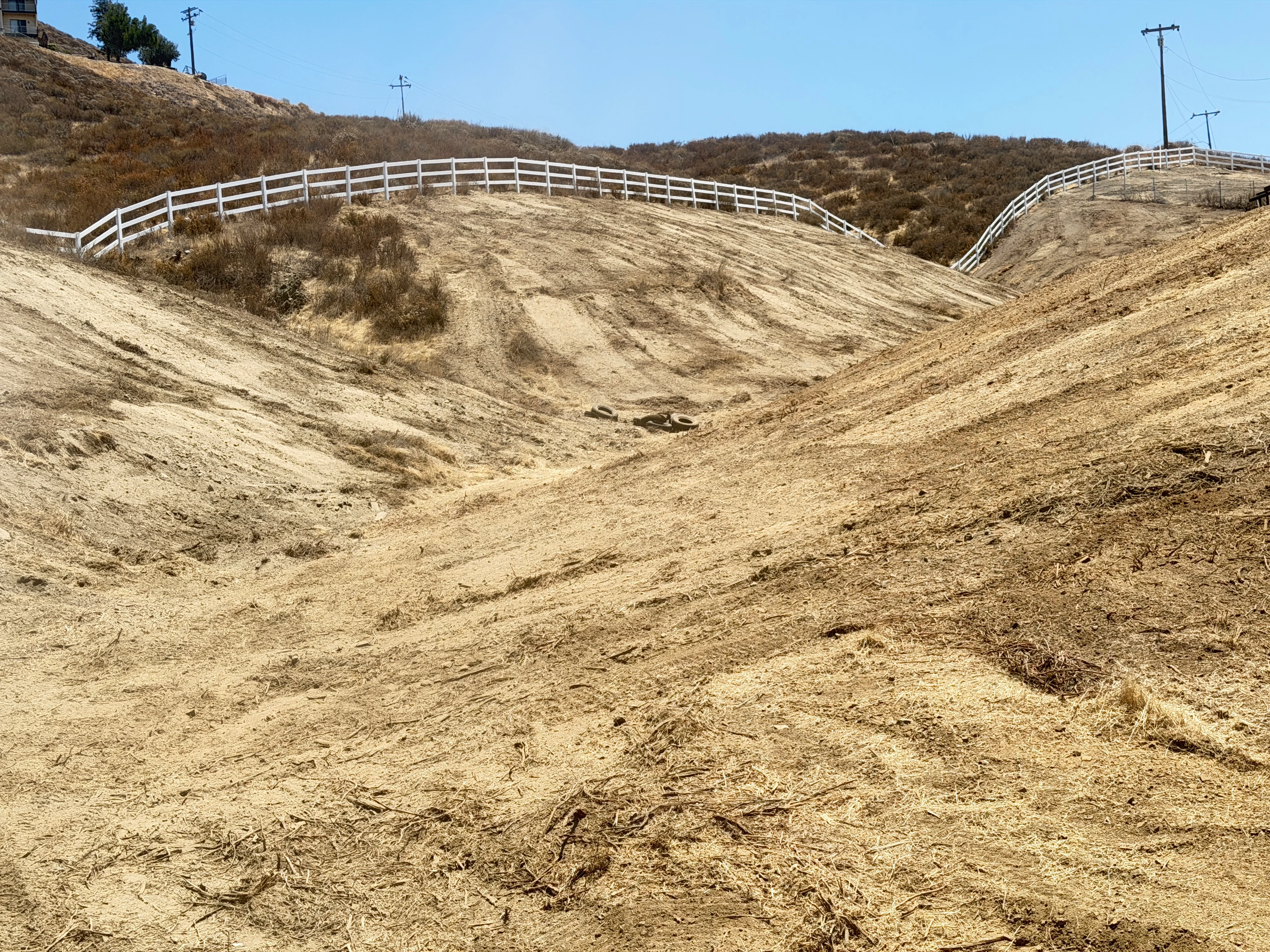 Cleared hillside with white ranch fencing installed along ridge, bare earth slopes visible