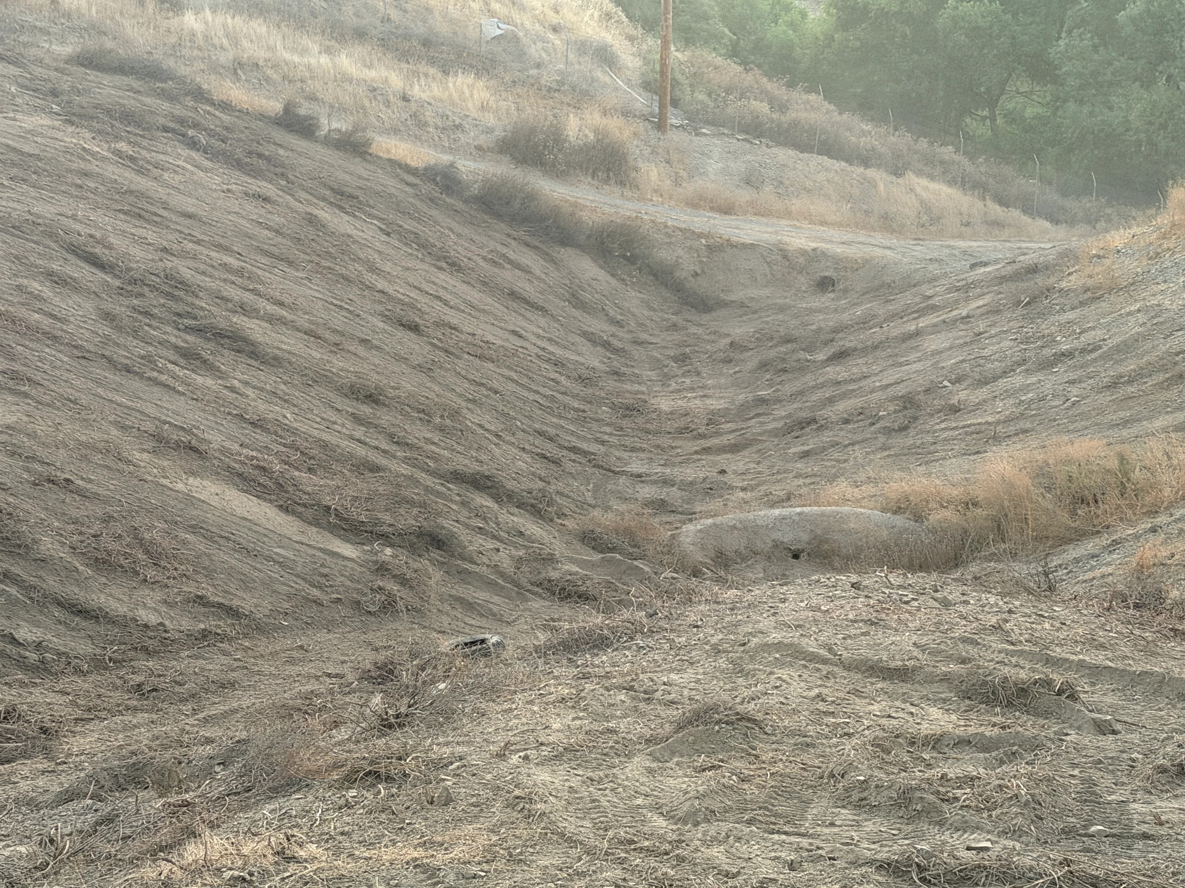Cleared hillside with graded slopes and remaining brush on upper terrain