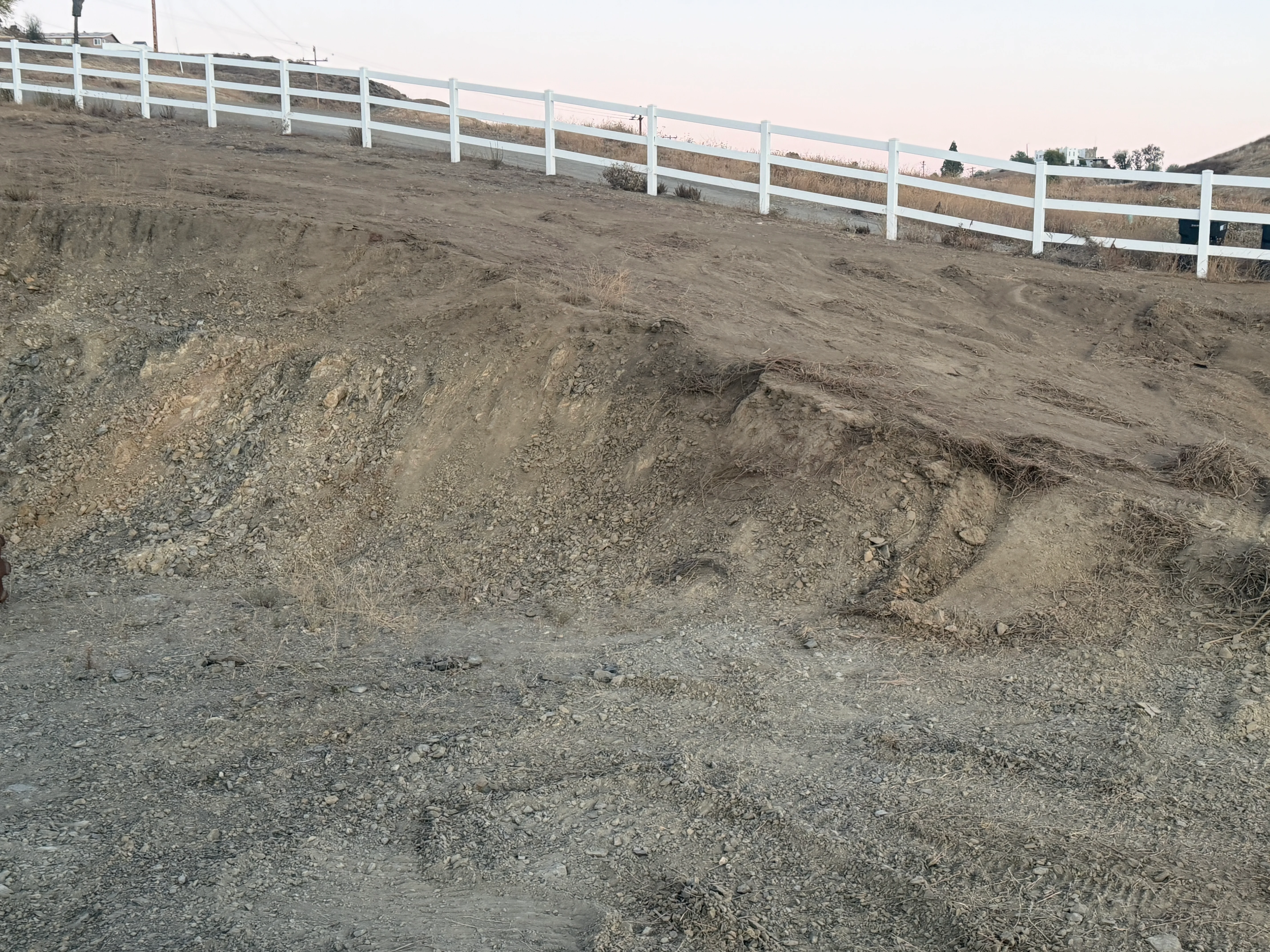 Cleared hillside property with exposed soil and white ranch fencing along the ridge