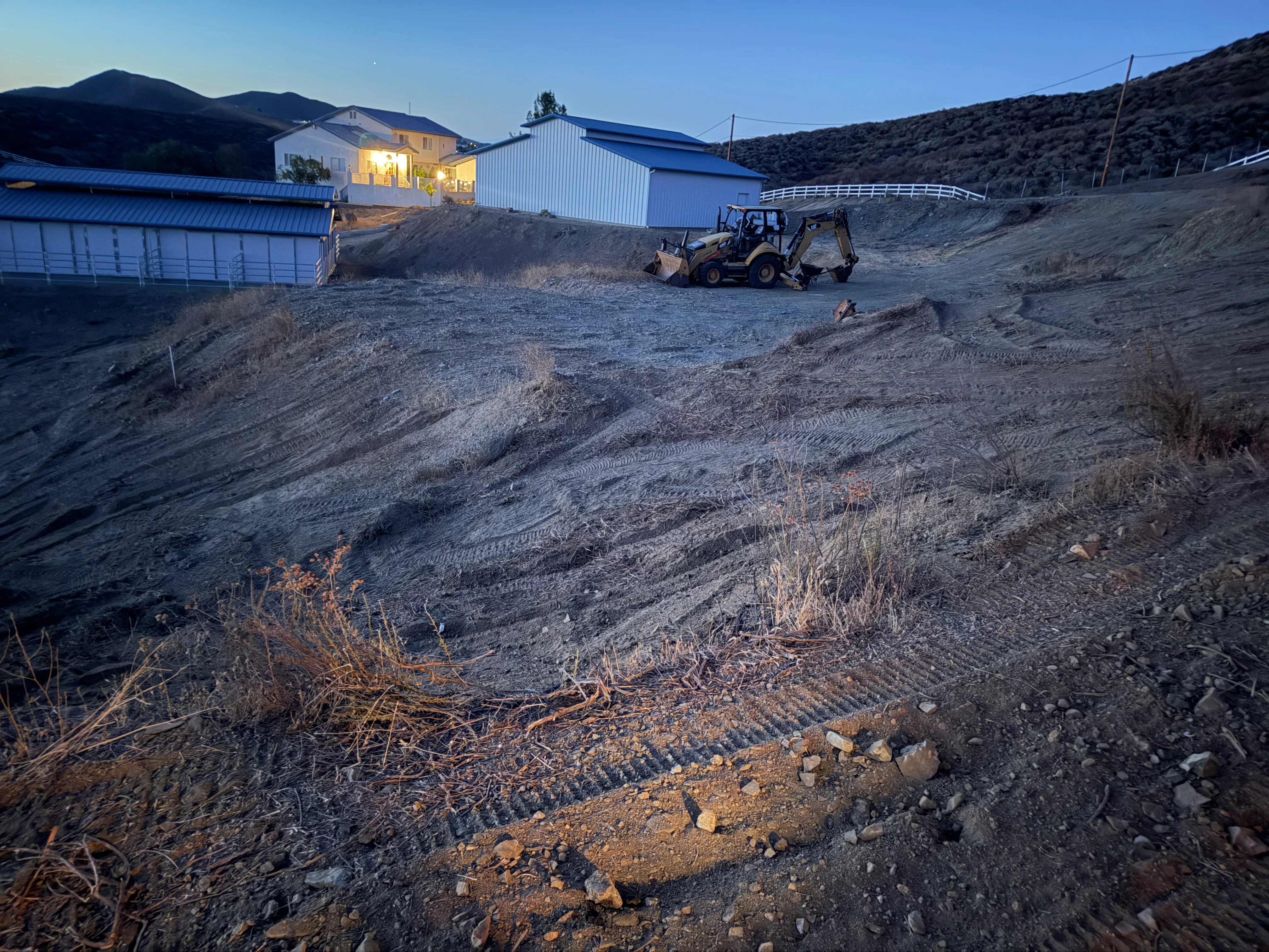 Cleared hillside with graded soil, erosion control, and wheel loader equipment at rural property