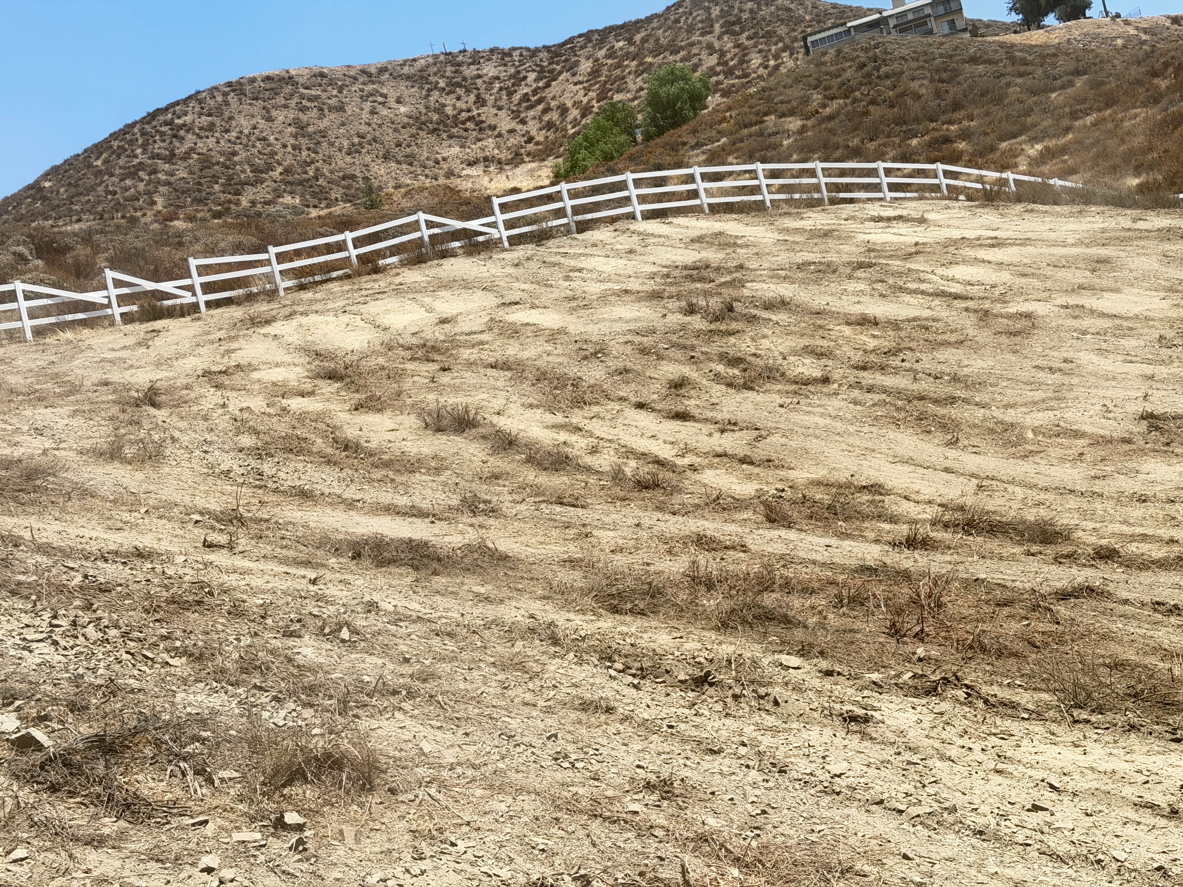 Cleared hillside with white ranch fencing installed along contoured slope