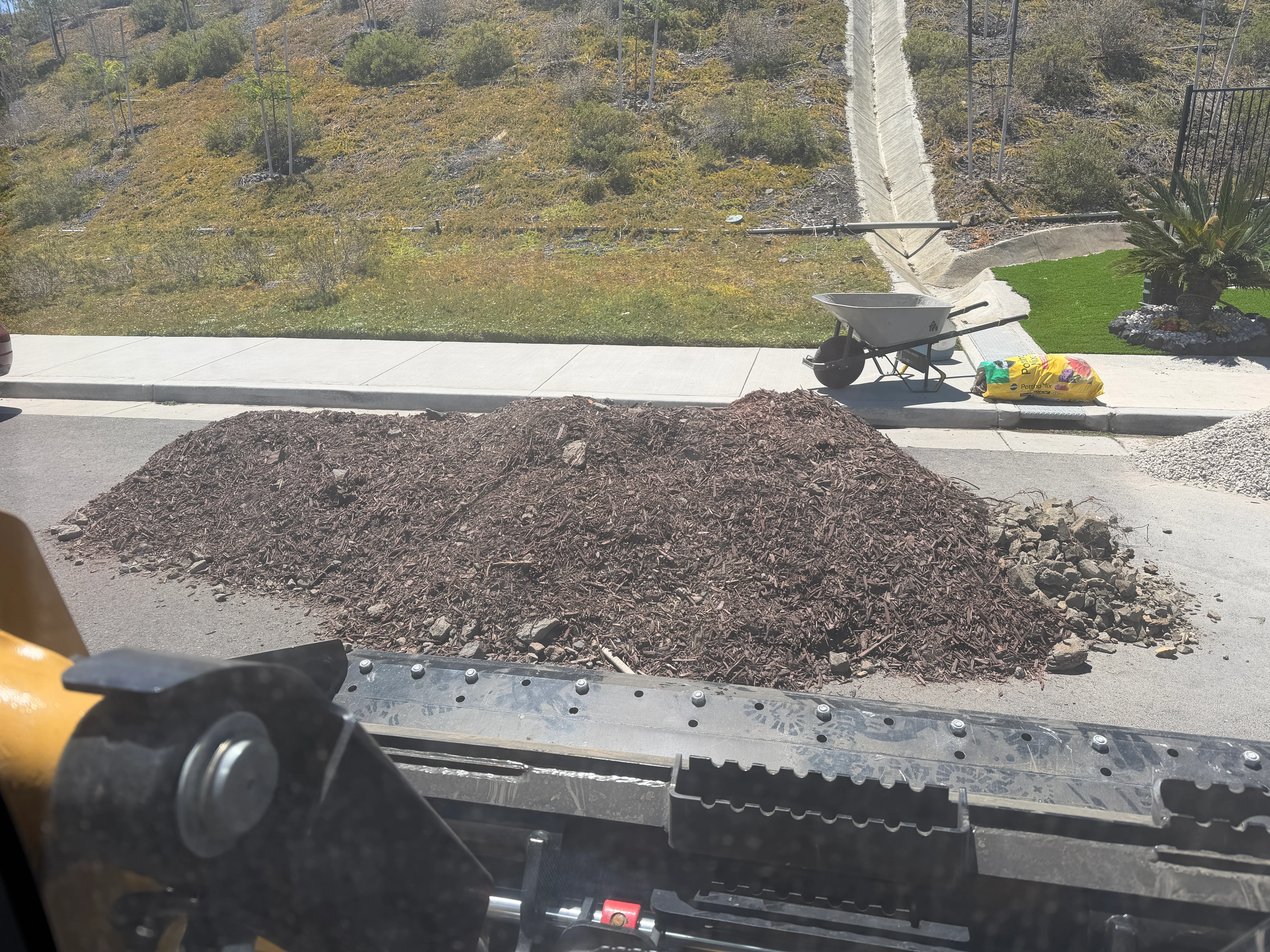 Hillside land clearing project with debris pile, concrete pad, and cleared landscaping area